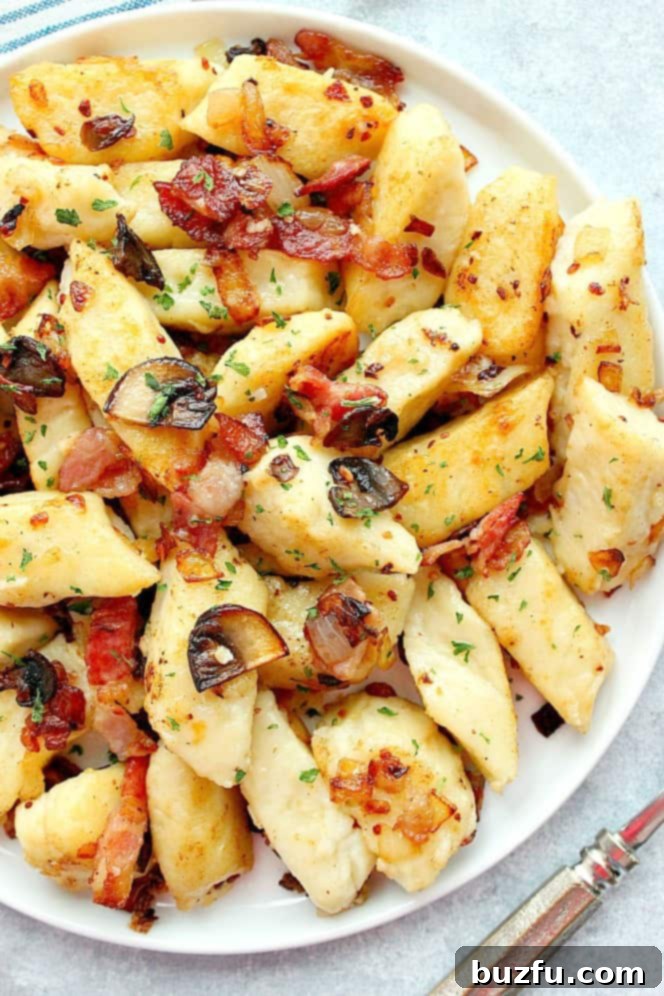 Overhead shot of Polish potato dumplings on white plate, with bacon and mushrooms, garnished with fresh parsley.