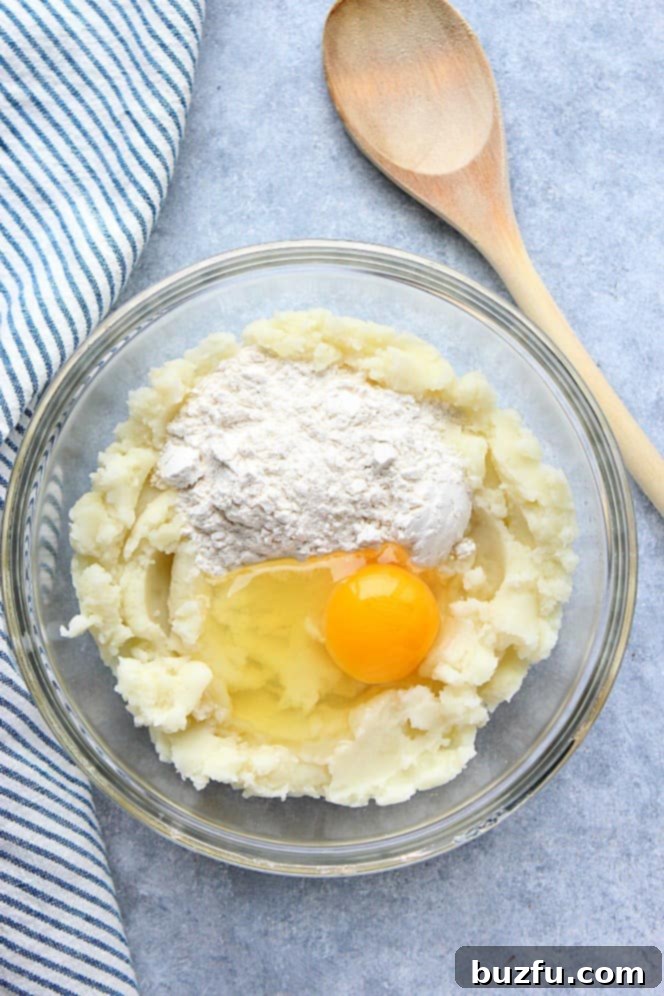 Overhead shot of mashed potatoes, egg, and flour in a glass bowl, ready for mixing.