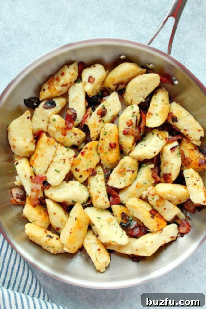 Overhead shot of Polish potato dumplings pan-frying to a golden brown in a stainless steel skillet, ready for toppings.