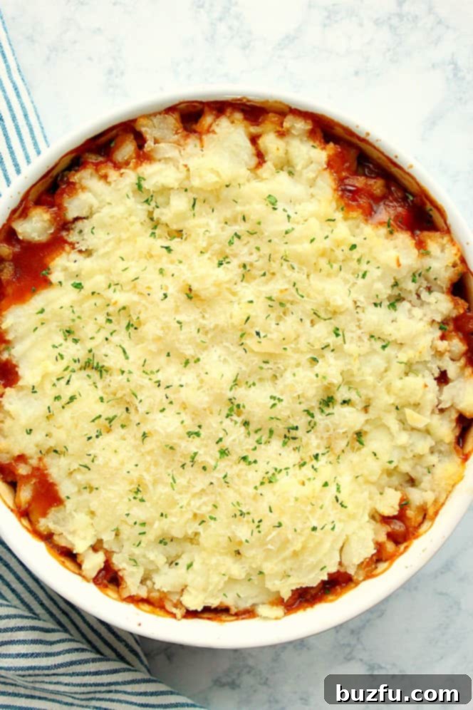 An inviting overhead shot of the baked vegetarian Shepherd's Pie in a round baking dish, topped with artfully piped mashed potatoes, golden brown and slightly crispy.