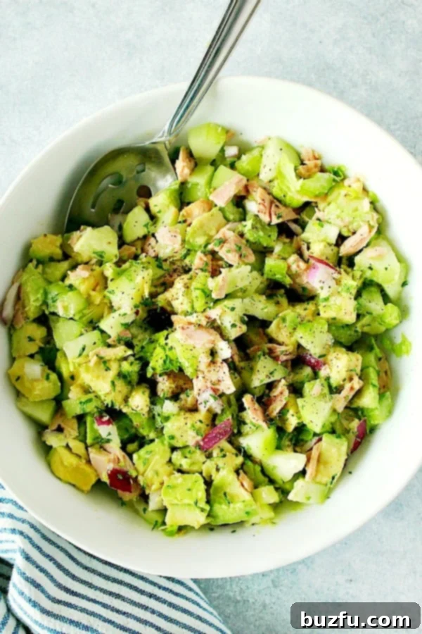 Avocado Tuna Salad Recipe - healthy and delicious salad made with ripe avocados, tuna, cucumber, celery and red onion. Perfect for sandwiches, wraps or eaten straight up! A large white bowl brimming with fresh Avocado Tuna Salad, ready to be served.