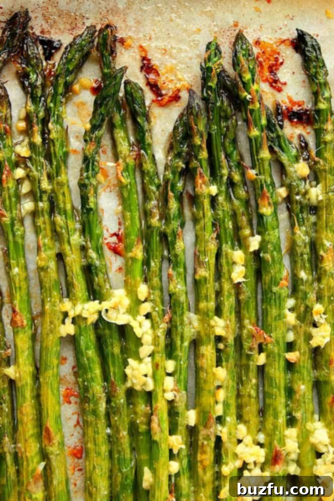 Overhead shot of freshly roasted asparagus Spears on parchment paper-lined baking sheet, garnished with lemon wedges and grated Parmesan.