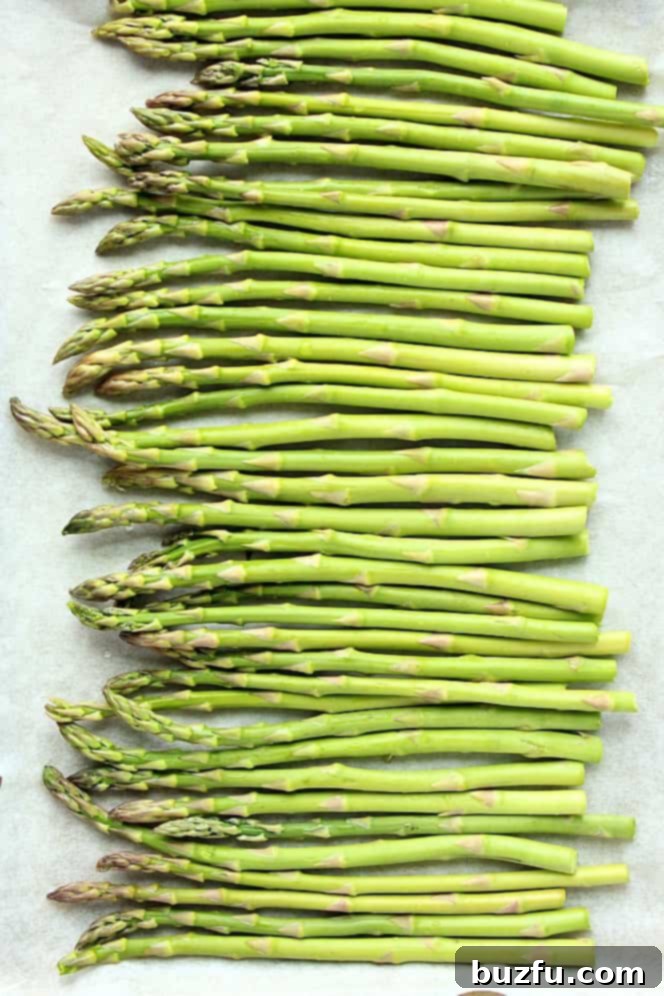 Overhead shot of fresh, uncooked asparagus spears arranged on a baking sheet lined with parchment paper, ready for roasting.