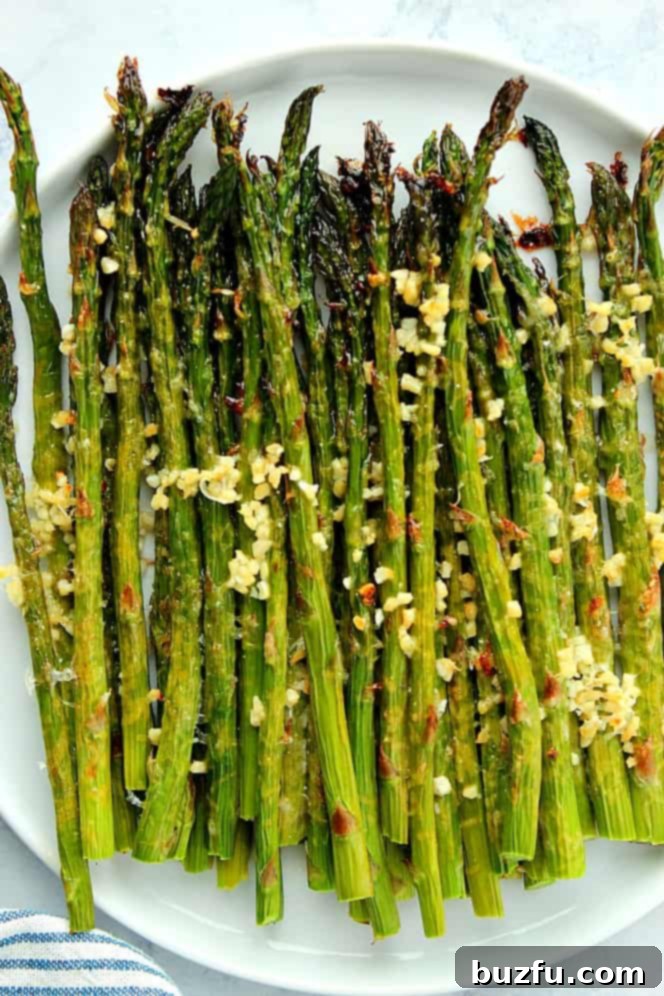Overhead shot of roasted garlic Parmesan asparagus on a white round plate, garnished with fresh lemon wedges.