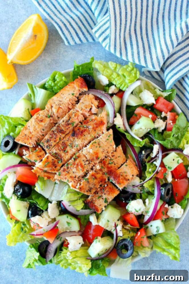 Overhead shot of Greek salad with sliced salmon on top, on plate, beautifully arranged for a healthy meal.