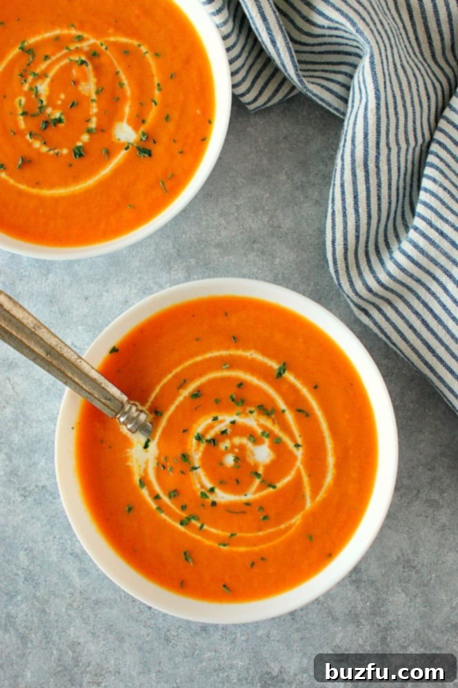 This delicious Creamy Carrot Soup is rich in flavor and absolutely delicious! This easy soup is bound to become a favorite! Overhead shot of creamy carrot soup in two bowls, garnished with fresh herbs, with a kitchen towel next to them.