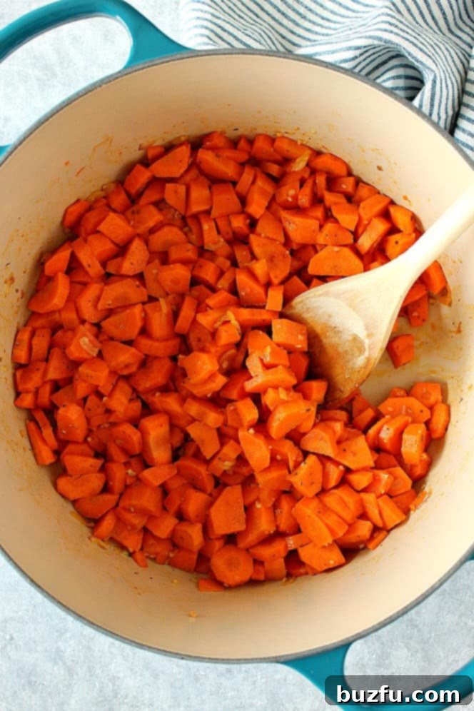 How to make creamy carrot soup. Dutch oven with chopped carrots inside, wooden spoon on the right.