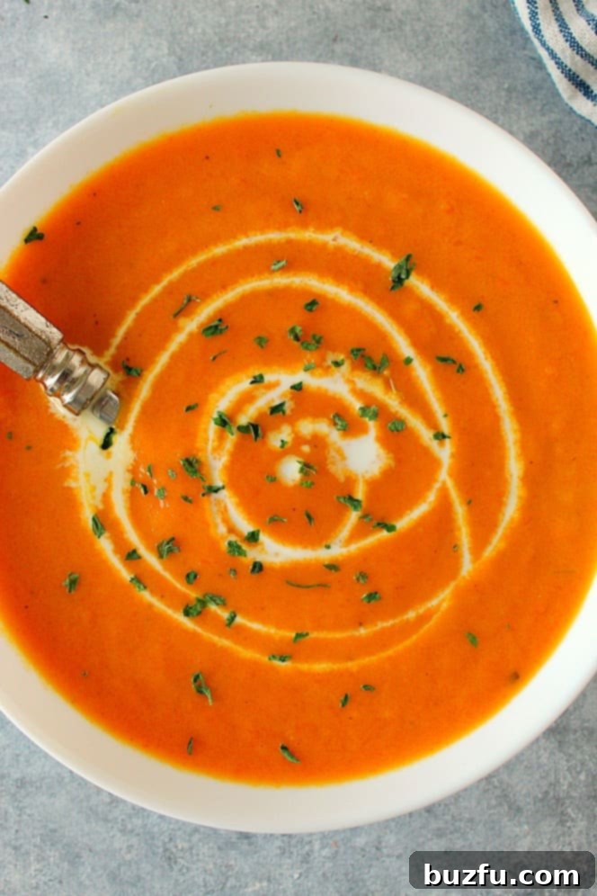 This delicious Creamy Carrot Soup is rich in flavor and absolutely delicious! This easy soup is bound to become a favorite! Overhead close up shot of creamy carrot soup in white bowl, with cream swirl on top.