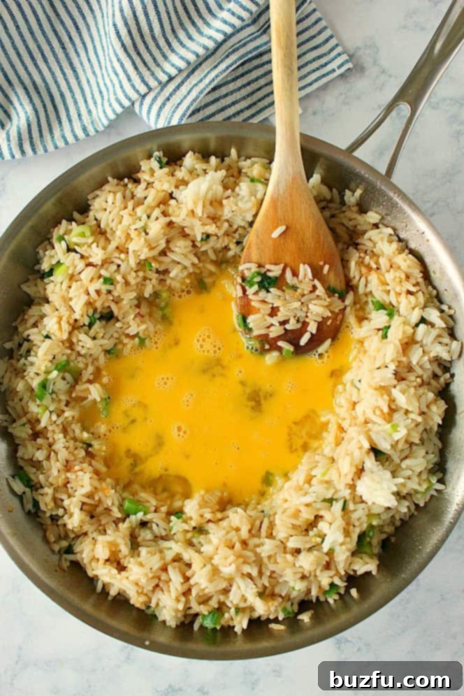 Overhead shot of rice in skillet, with beaten eggs in the center of the pan, about to be mixed.