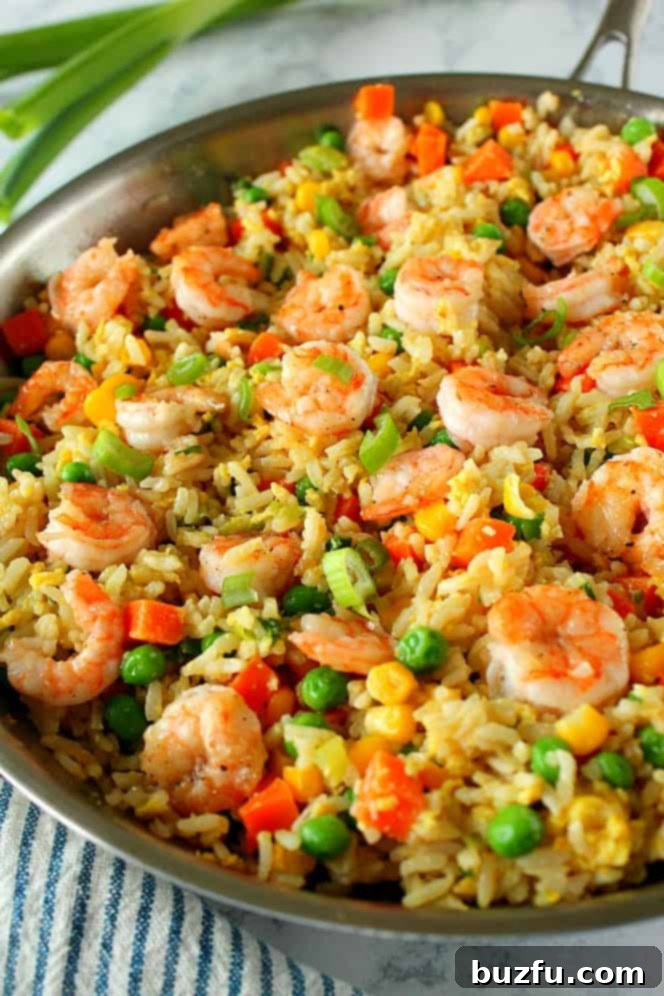 Side close up shot of vibrant shrimp fried rice with green onions in a stainless steel pan.