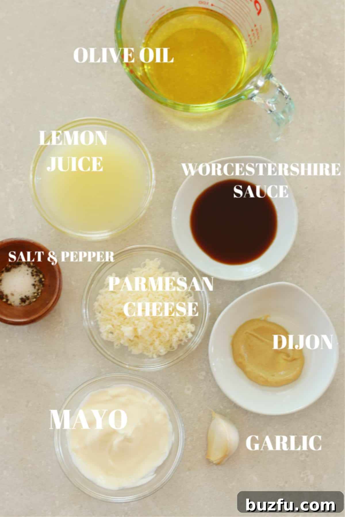 All ingredients for the Caesar salad dressing laid out in small bowls on a gray cutting board.