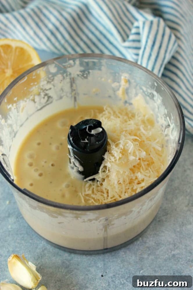 Side shot of Caesar dressing in a mini food processor with grated Parmesan cheese being added.