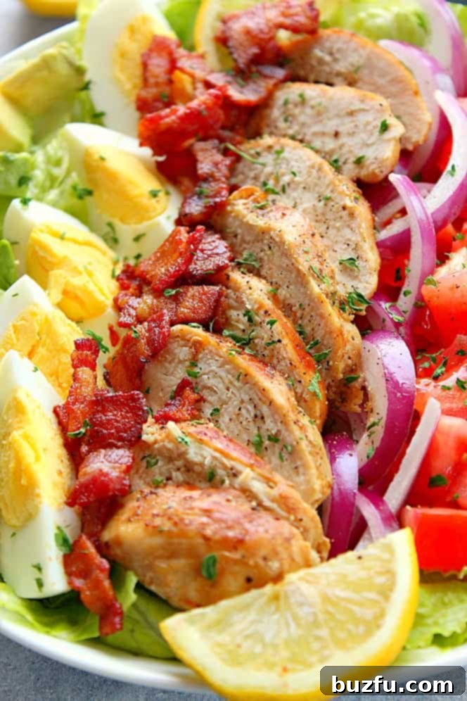 Chicken Cobb Salad with juicy lemon garlic chicken, crispy bacon, eggs, tomatoes, avocado, onion, lettuce and simple Dijon dressing. This whole-meal salad is perfect for lunch or dinner! Side shot of chicken Cobb salad with bacon, eggs, onion and tomatoes, showing the distinct layers of ingredients.