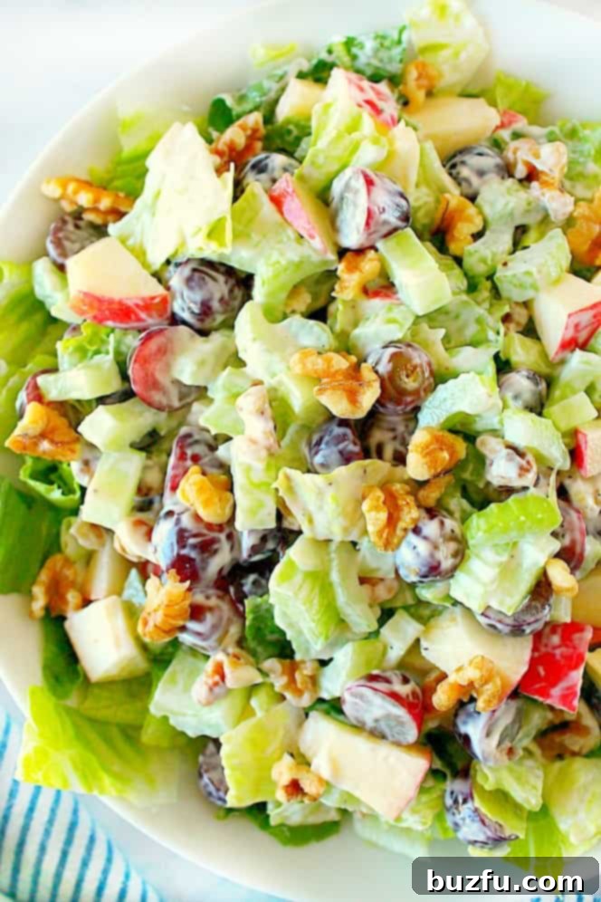 Creamy Classic Waldorf Salad: Fresh Apples, Grapes, Walnuts, and Celery in a Tangy Dressing. Overhead shot of creamy Waldorf salad, in white bowl, garnished with a few grapes and walnut halves.