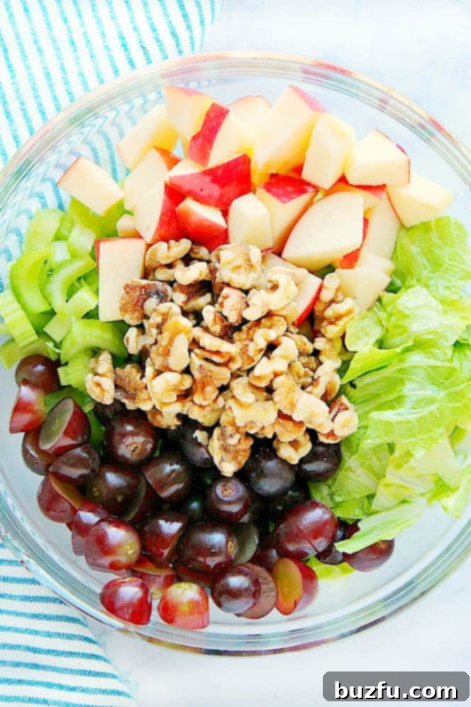 Prepping for Classic Waldorf Salad: Freshly Chopped Ingredients in a Bowl. Overhead shot of chopped apples, walnuts, celery, grapes and lettuce in glass mixing bowl, ready to be tossed.