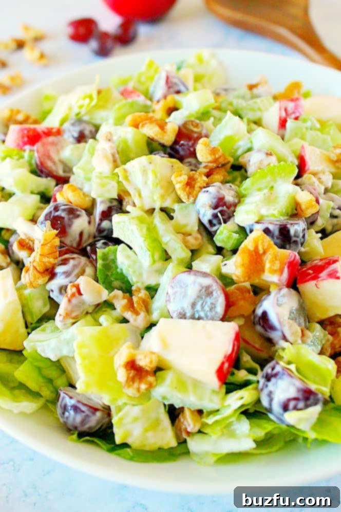 Ready-to-Serve Classic Waldorf Salad: A Refreshing and Flavorful Dish. Side shot of Waldorf salad in a white bowl, with a wooden salad spoon on the side, ready to be served.
