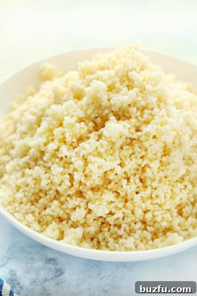 Side shot of cooked couscous in white bowl, garnished with fresh herbs.