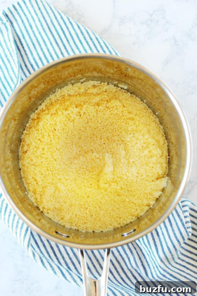Overhead shot of couscous in water in a stainless steel pot, just before covering.
