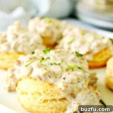 The Ultimate Creamy Sausage Gravy 3 Fluffy biscuits on a white plate, some generously covered with homemade sausage gravy.