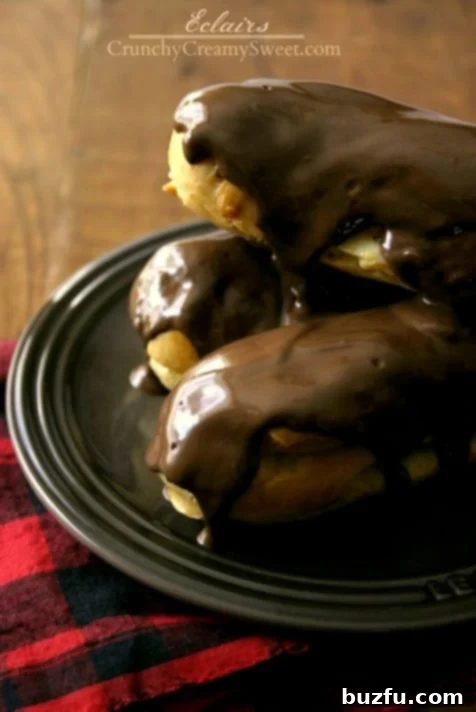 Side shot of eclairs stacked on each other on brown plate, filled with creamy custard and topped with melted chocolate.