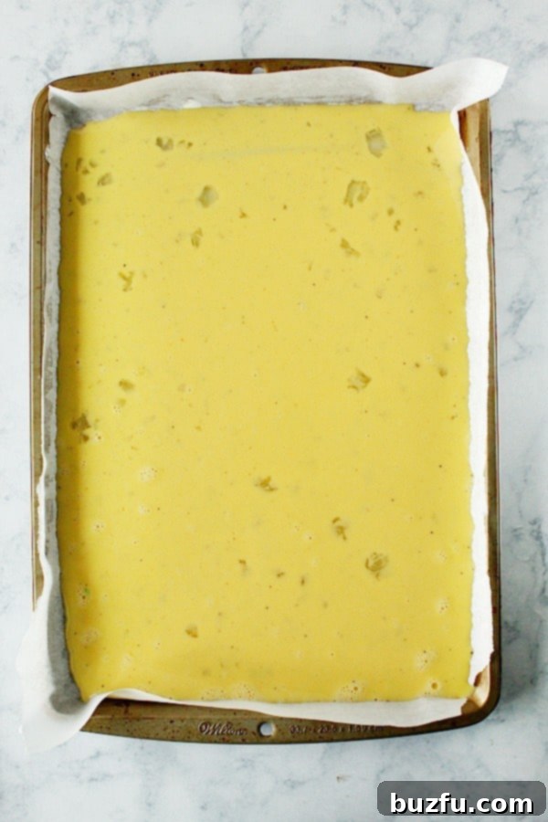 Unbaked egg mixture in a parchment-lined sheet pan, ready for the oven to create easy breakfast sandwich eggs.