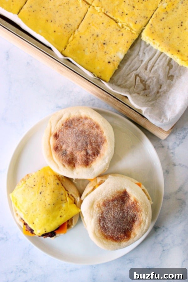 Assembling freezer breakfast sandwiches on a white plate, showing layers of English muffin, cheese, sausage, and egg.