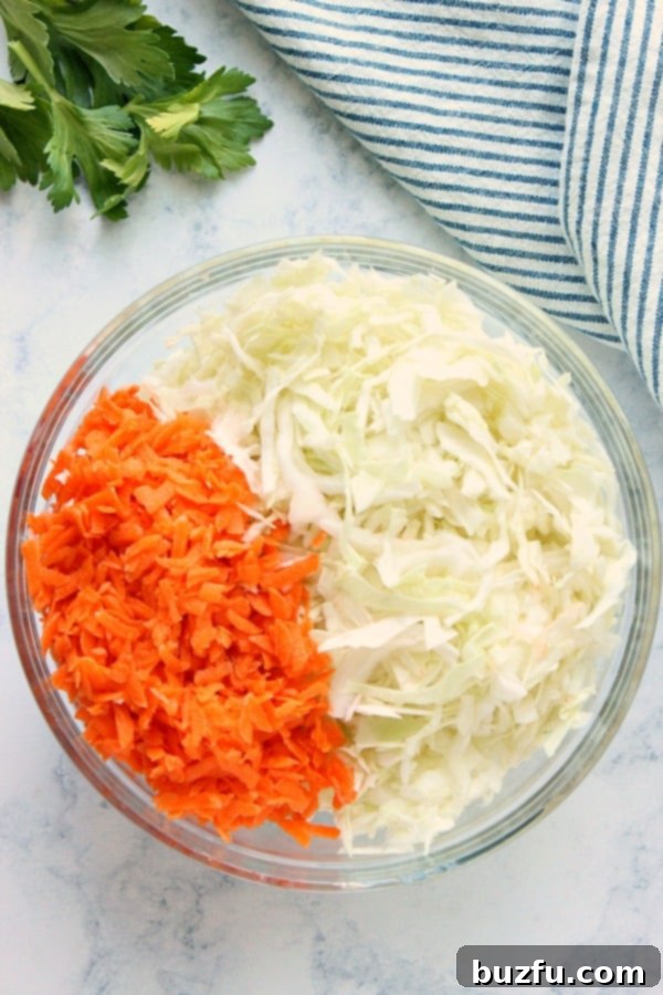 Shredded cabbage and carrots in a clear glass bowl, ready for the dressing.