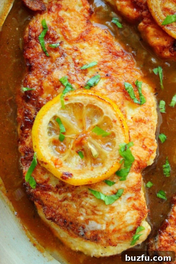 Close up on Chicken Francese in sauce in pan, showcasing golden brown chicken and vibrant lemon sauce.
