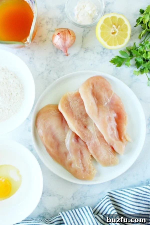 Chicken Francese ingredients neatly arranged on a marble board, including chicken, flour, eggs, lemons, butter, and a shallot.
