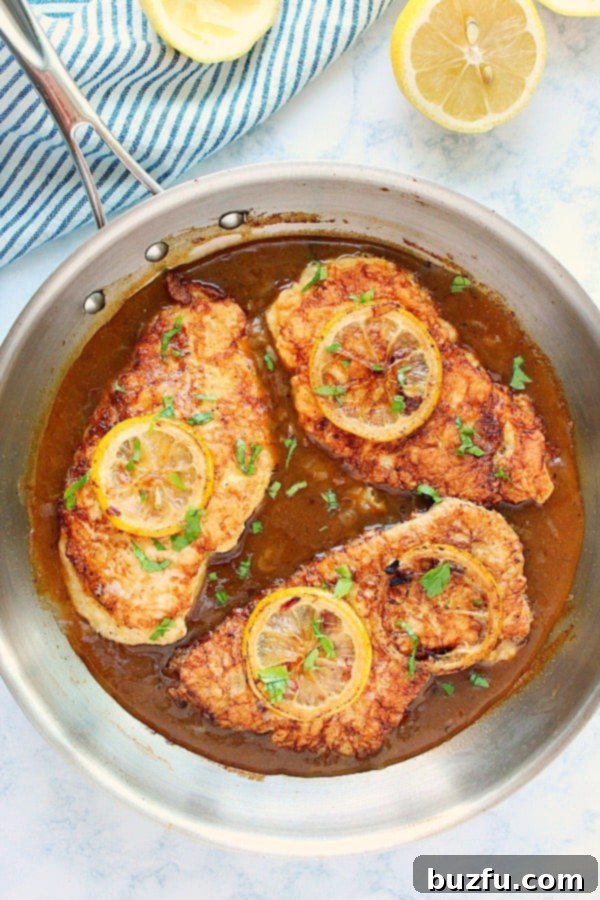 Three Chicken Francese pieces perfectly cooked and glistening in lemon butter sauce in a stainless steel pan.