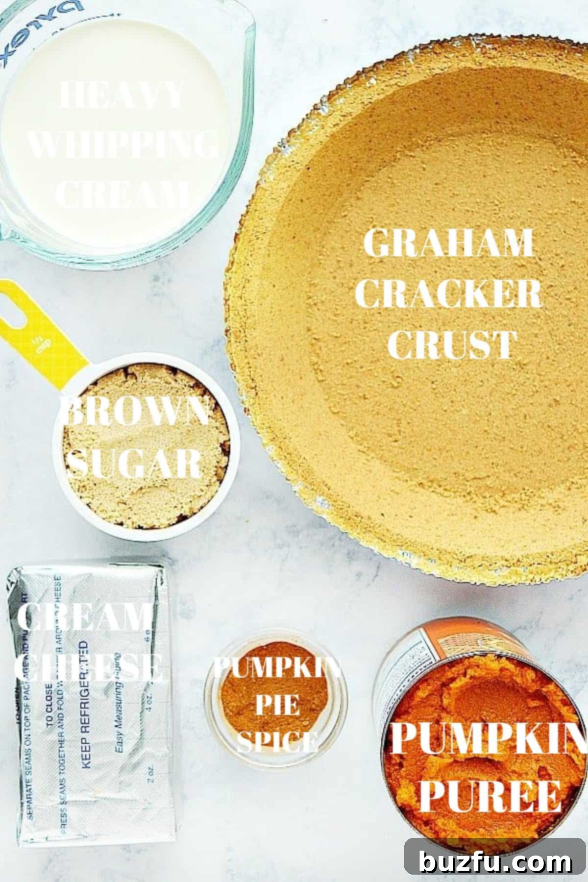 Key ingredients for No-Bake Pumpkin Pie: graham cracker crust, pumpkin puree, cream cheese, brown sugar, pumpkin pie spice, and heavy cream arranged on a marble board.