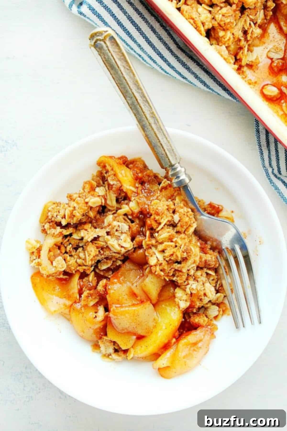 A generous serving of Old-Fashioned Apple Crisp in a white bowl, topped with melting caramel ice cream.