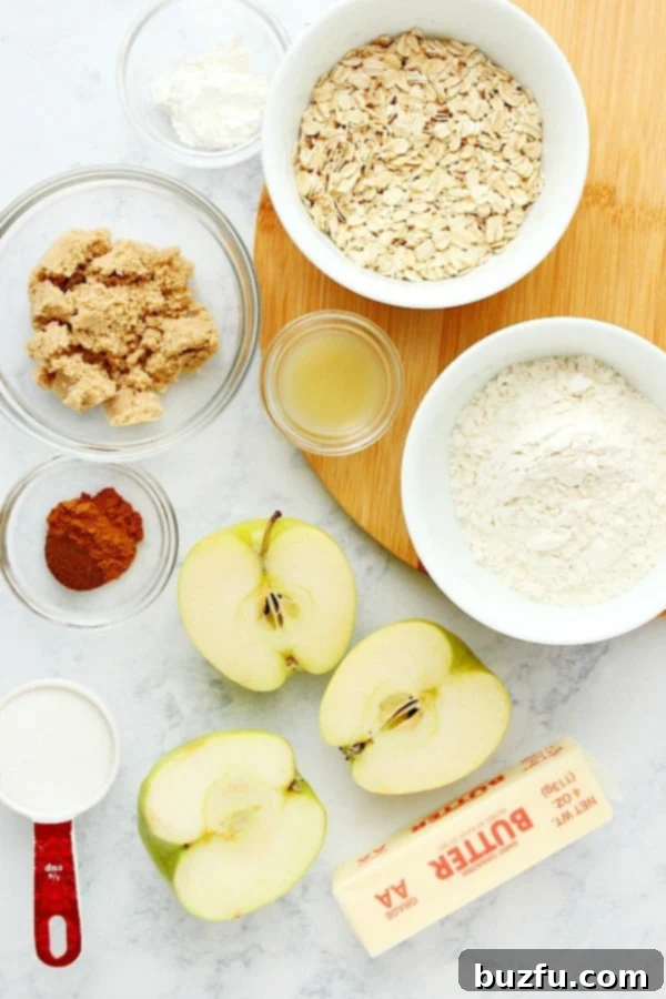 Various fresh ingredients for apple crisp laid out on a marble board, including apples, oats, sugar, and spices.