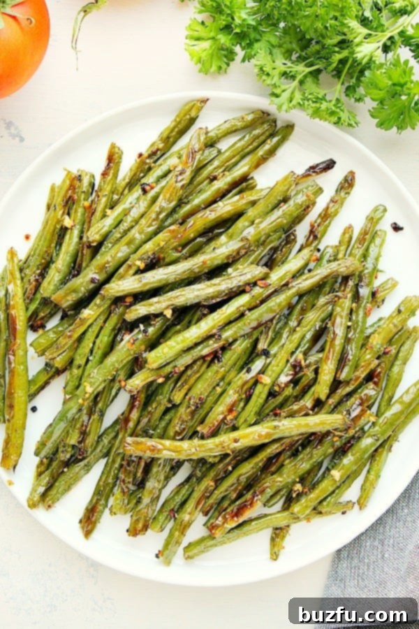 A serving of perfectly roasted green beans on a white plate, garnished with fresh herbs.