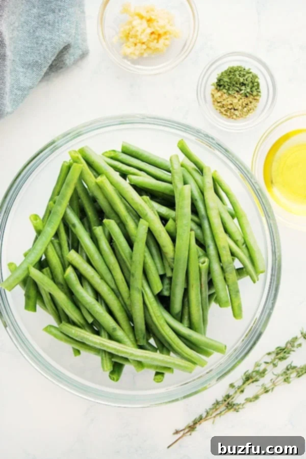 Fresh green beans, garlic, olive oil, and Italian seasoning laid out on a marble board, ready for roasting.