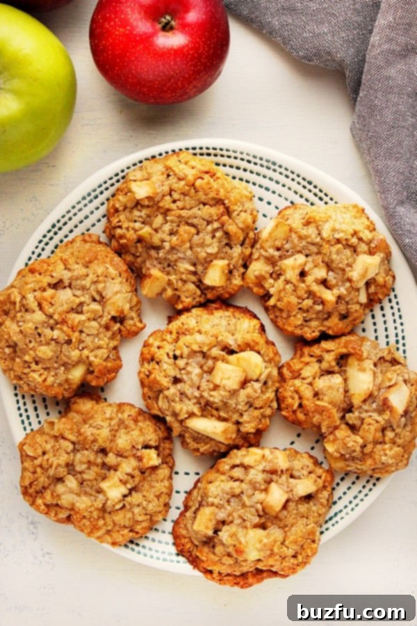 Enjoy these delightful Apple Cinnamon Oatmeal Cookies with sweet apple chunks for a perfect seasonal treat. A stack of perfectly baked Apple Cinnamon Oatmeal Cookies on a white plate, garnished with fresh apple slices, highlighting the rich texture and comforting fall flavors.