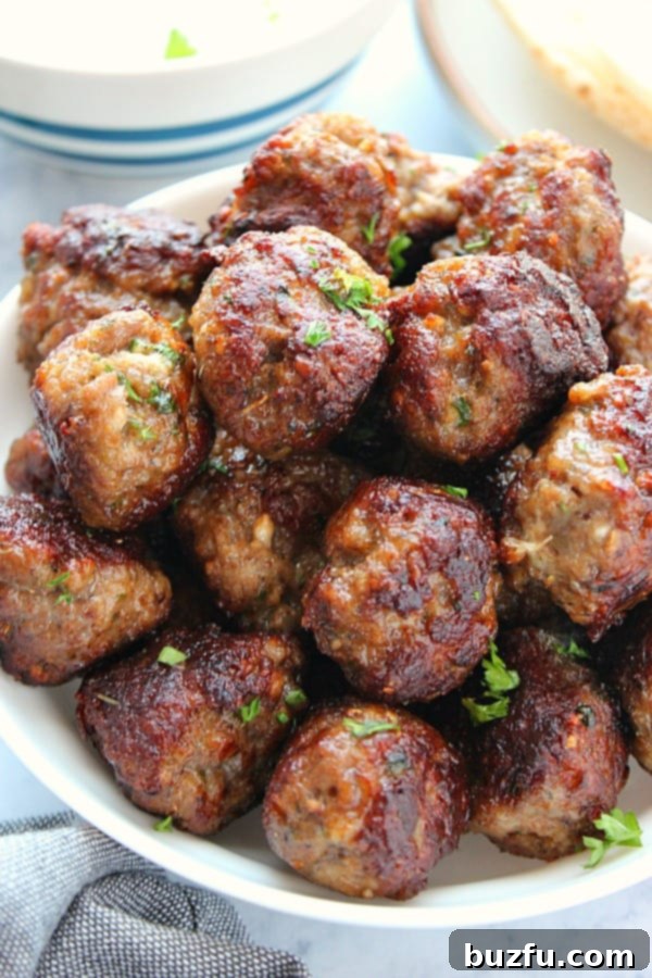 Authentic Greek Meatballs (Keftedes) are perfectly seasoned and made with ground lamb or other meats. Juicy Greek Meatballs (Keftedes) in a white serving bowl, garnished with fresh herbs, ready to be enjoyed.