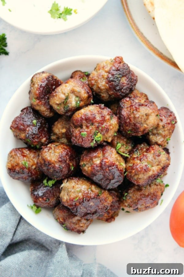 Enjoy the best Greek Meatballs with homemade Tzatziki Sauce or a rich tomato sauce. A serving of Greek meatballs in a white bowl, accompanied by a side of fresh cucumber garlic Tzatziki sauce, perfect for dipping.