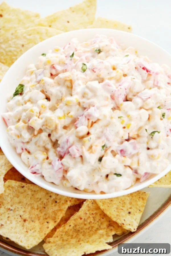 How to make quick and easy Cold Corn Dip. Creamy Corn Dip served in a white bowl, surrounded by a generous amount of tortilla chips.