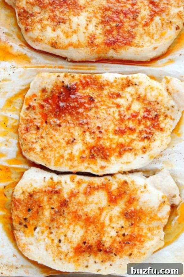 Herb-Crusted Baked Pork Chops 5 Three golden-brown baked pork chops resting on a parchment paper-lined baking sheet.