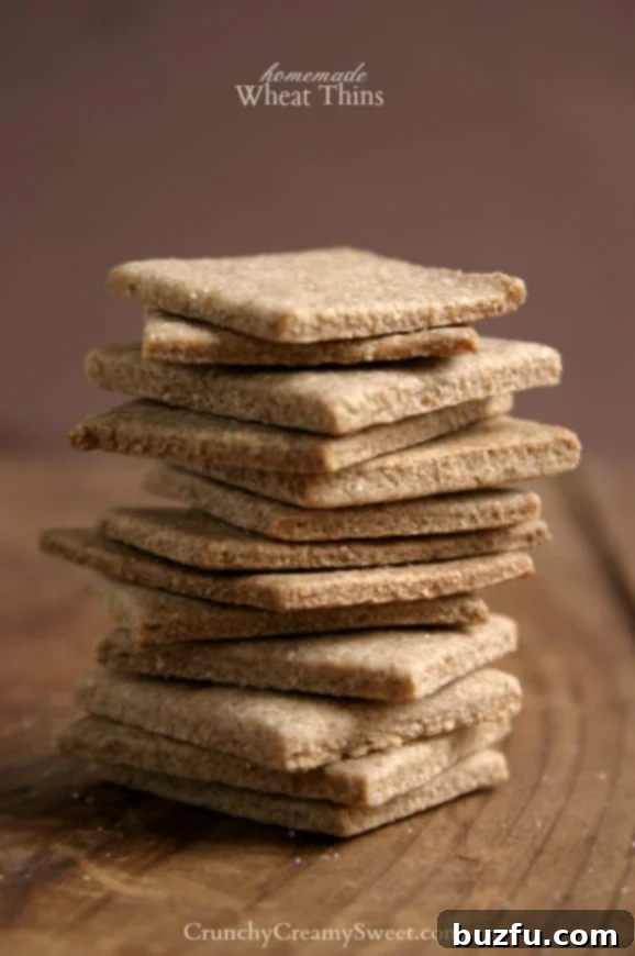 A stack of golden brown homemade Wheat Thins crackers on a rustic wooden board, ready to be enjoyed.