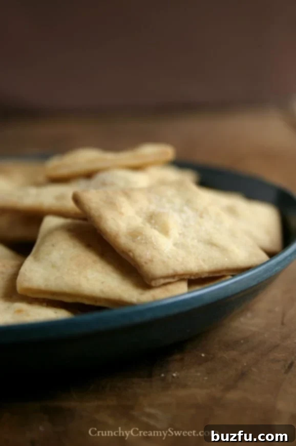 Close-up of golden-brown homemade crackers on a white plate, placed on a rustic wooden board, emphasizing their crispy texture.