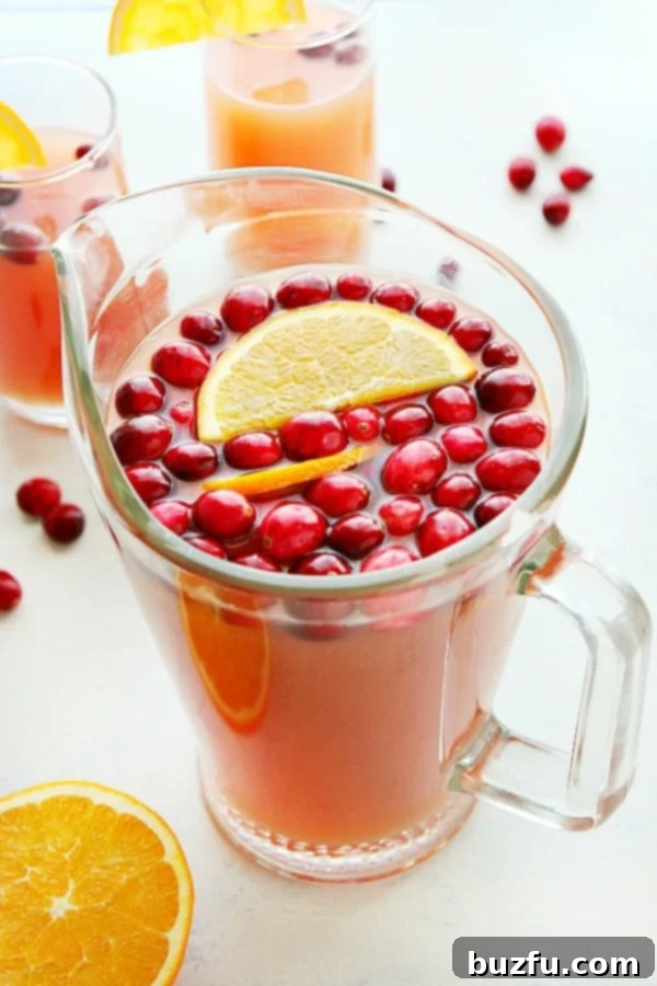 Vibrant Christmas Punch in a clear glass pitcher, garnished with fresh cranberries and orange slices, ready for holiday festivities.