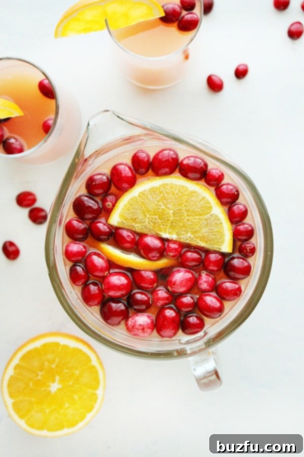 Close-up of cranberry punch in a pitcher, featuring the vibrant red liquid, floating fresh cranberries, and bright orange slices for garnish.