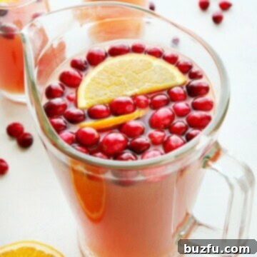 A glass pitcher filled with festive Christmas Punch, garnished with fresh cranberries and orange slices.
