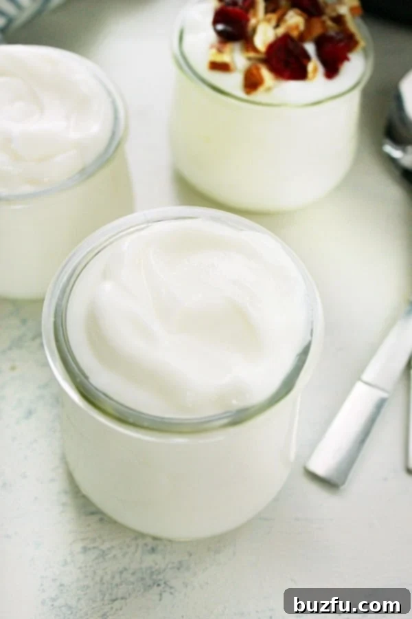 Four small glass jars of Instant Pot yogurt with various toppings like berries, nuts, and honey, displayed on a wooden board.
