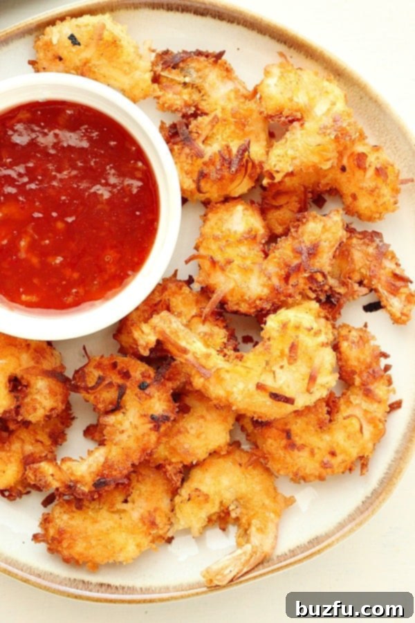 Crispy homemade Coconut Shrimp served on a white plate with a side of vibrant Sweet Chili Orange Dipping Sauce, garnished with fresh herbs.