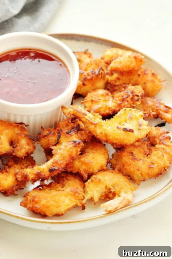 A beautifully arranged plate of golden, crispy coconut shrimp with a vibrant dipping sauce in a small bowl, garnished with fresh herbs.