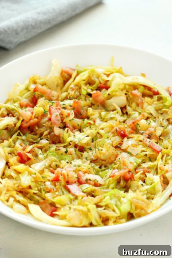 A serving of delicious Fried Cabbage with Bacon in a white bowl, garnished with fresh herbs.