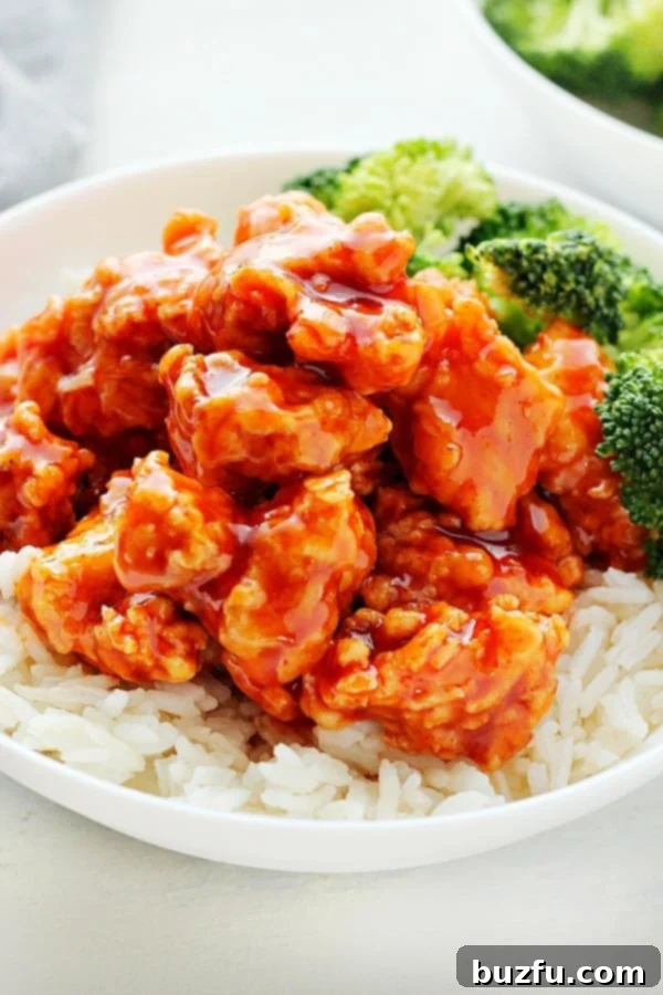 A bowl of crispy Korean Fried Chicken with Gochujang sauce served over white rice, garnished with sesame seeds and green onions.